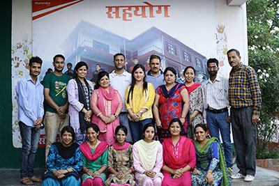 People standing in front of a school banner with a row of people sitting in front of them